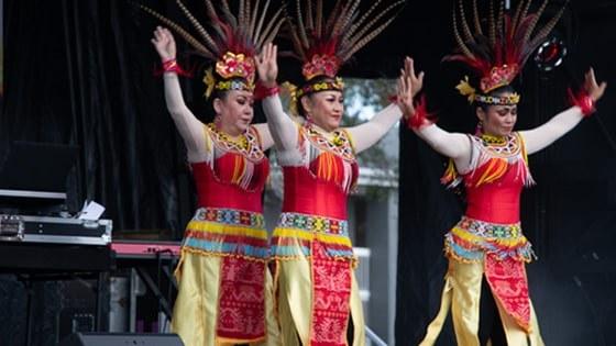 三个女人戴着五颜六色的印尼羽毛头饰跳舞, 黄色的裙子, 还有串珠腰带和衣领.